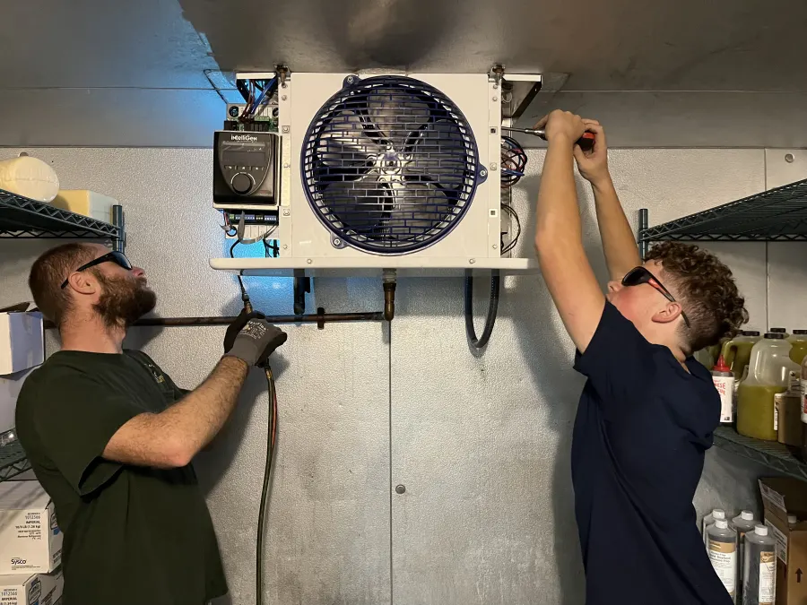 Two DG Service technicians installing an evaporator fan unit inside a walk-in cooler